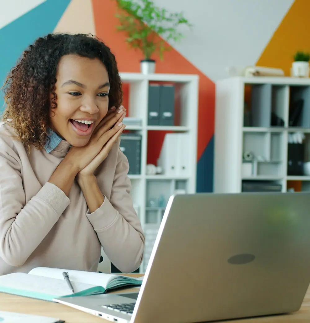 A woman delighted by something on her laptop, a mug beside her